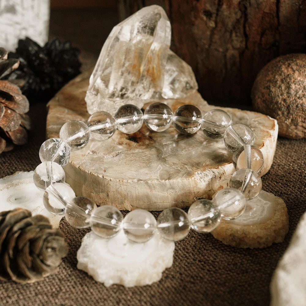 Clear beaded bracelet on a wooden surface with crystals and pinecones