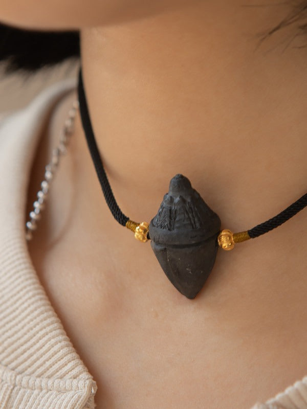 Close view of handmade tsatsa pendant on black braided cord